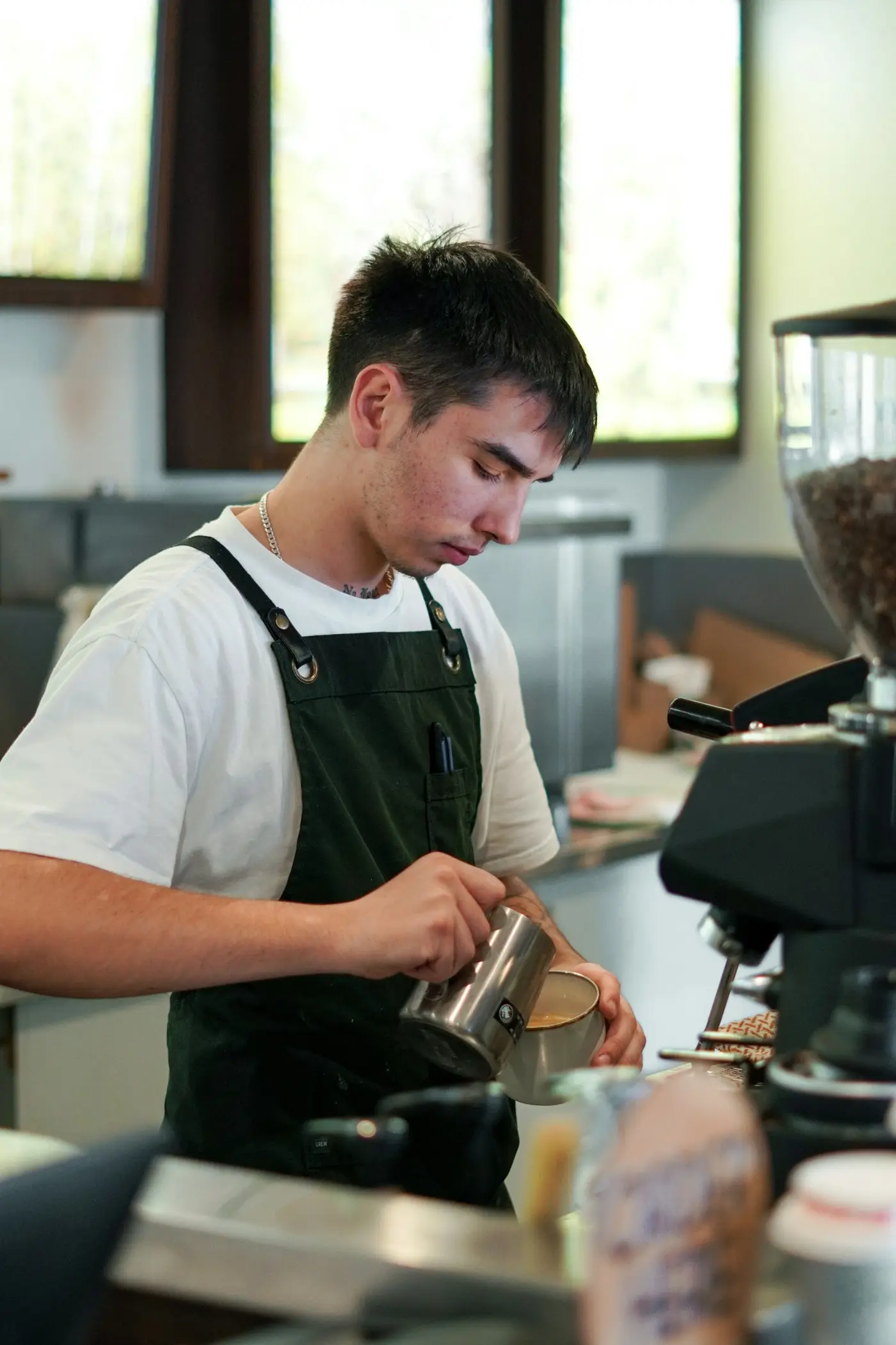 Barista in zwart schort die melk opschuimt achter de espressomachine
